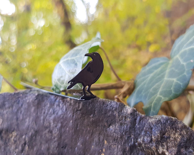 Black metal raven-shaped page saver perched on a rock with ivy leaves in the background. A mystical, forest-inspired gift for readers drawn to folklore and dark nature aesthetics.
