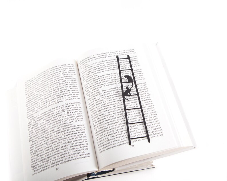 Black metal bookmark Cat on the Ladder. Two cats are sitting on the ladder, which is the size of an average book. The ladder stays between the pages of the book. The tips of the ladder are on the side of the book.