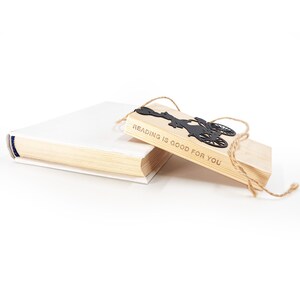 Black metal bike bookmark resting on a wooden block engraved with “Reading is good for you,” placed on a closed book with natural twine packaging on a white background.