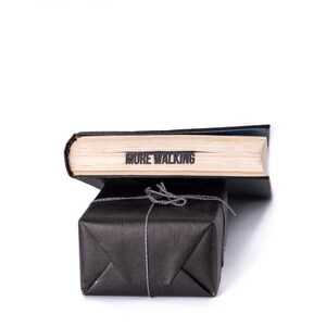 May include: A black book wrapped in black paper with a string bow. The book has the words "MORE WALKING" printed on the spine.
