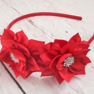 May include: Red fabric flower headband with a rhinestone center. The headband is made of a thin, flexible material.