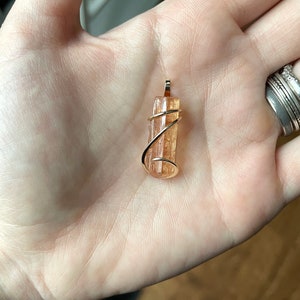 May include: A gold wire wrapped pendant featuring a natural, orange-brown, translucent crystal.