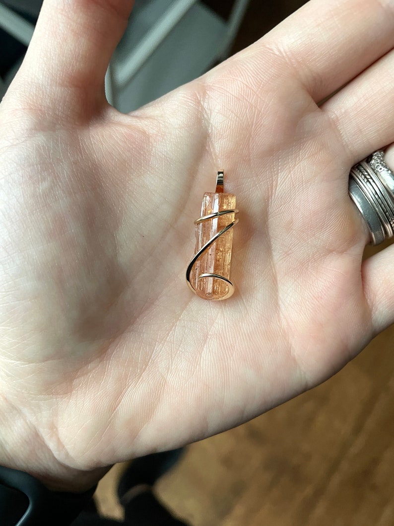 May include: A gold wire wrapped pendant featuring a natural, orange-brown, translucent crystal.