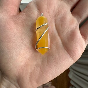 Pu&ograve; includere: Un punto di cristallo giallo avvolto in filo d'argento, creando un ciondolo.