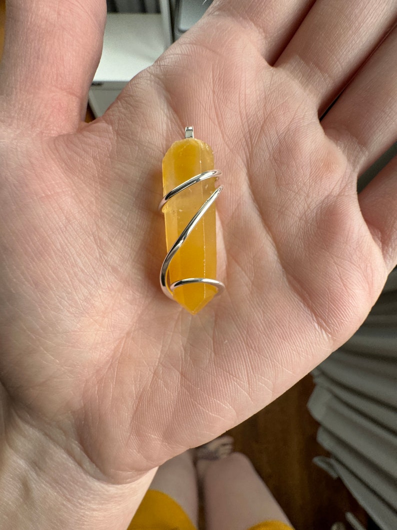 Pu&ograve; includere: Un punto di cristallo giallo avvolto in filo d'argento, creando un ciondolo.
