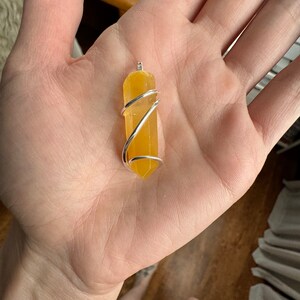 Pu&ograve; includere: Un ciondolo di cristallo giallo avvolto in filo d'argento. Il ciondolo ha una forma rettangolare lunga e sottile, con un'estremit&agrave; appuntita.