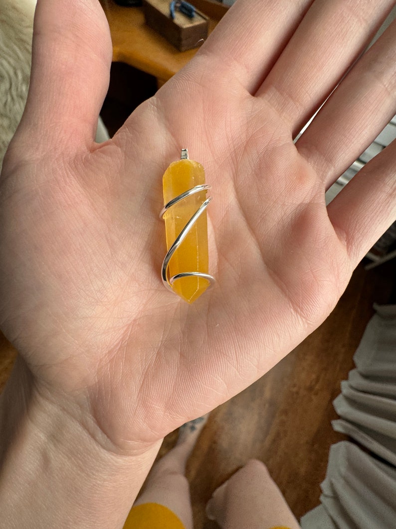 Pu&ograve; includere: Un ciondolo di cristallo giallo avvolto in filo d'argento. Il ciondolo ha una forma rettangolare lunga e sottile, con un'estremit&agrave; appuntita.