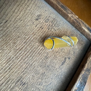 Pu&ograve; includere: Un cristallo giallo avvolto da un anello di filo d'argento. Il cristallo &egrave; su una superficie di legno.
