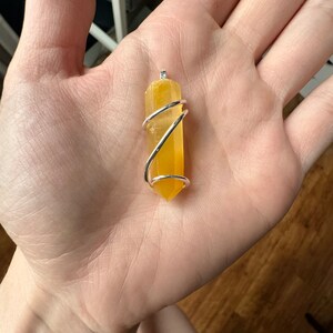 Pu&ograve; includere: Un punto di cristallo giallo avvolto in filo d'argento, creando un ciondolo.