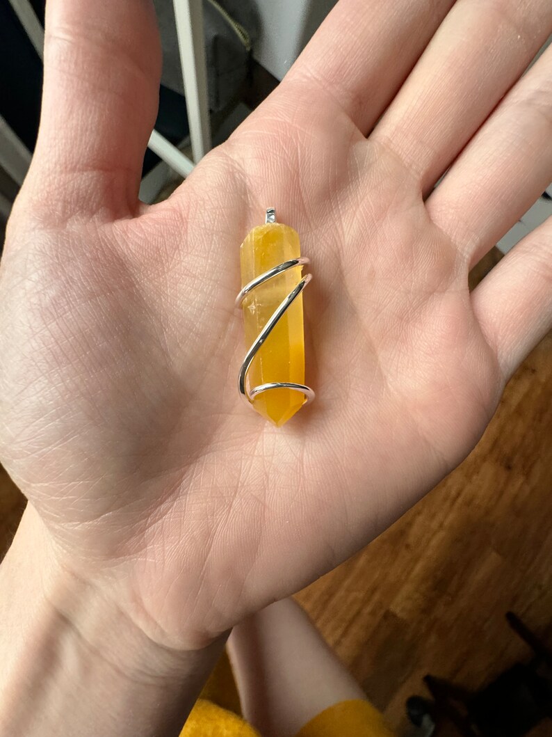 Pu&ograve; includere: Un punto di cristallo giallo avvolto in filo d'argento, creando un ciondolo.