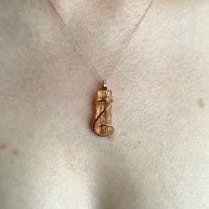 May include: A gold necklace with a pendant featuring a wrapped, clear, orange, and brown crystal.