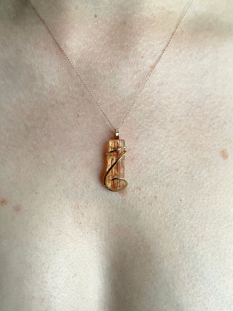 May include: A gold necklace with a pendant featuring a wrapped, clear, orange, and brown crystal.
