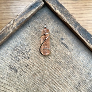 May include: A brown and white crystal pendant wrapped in silver wire. The pendant is on a wooden surface.
