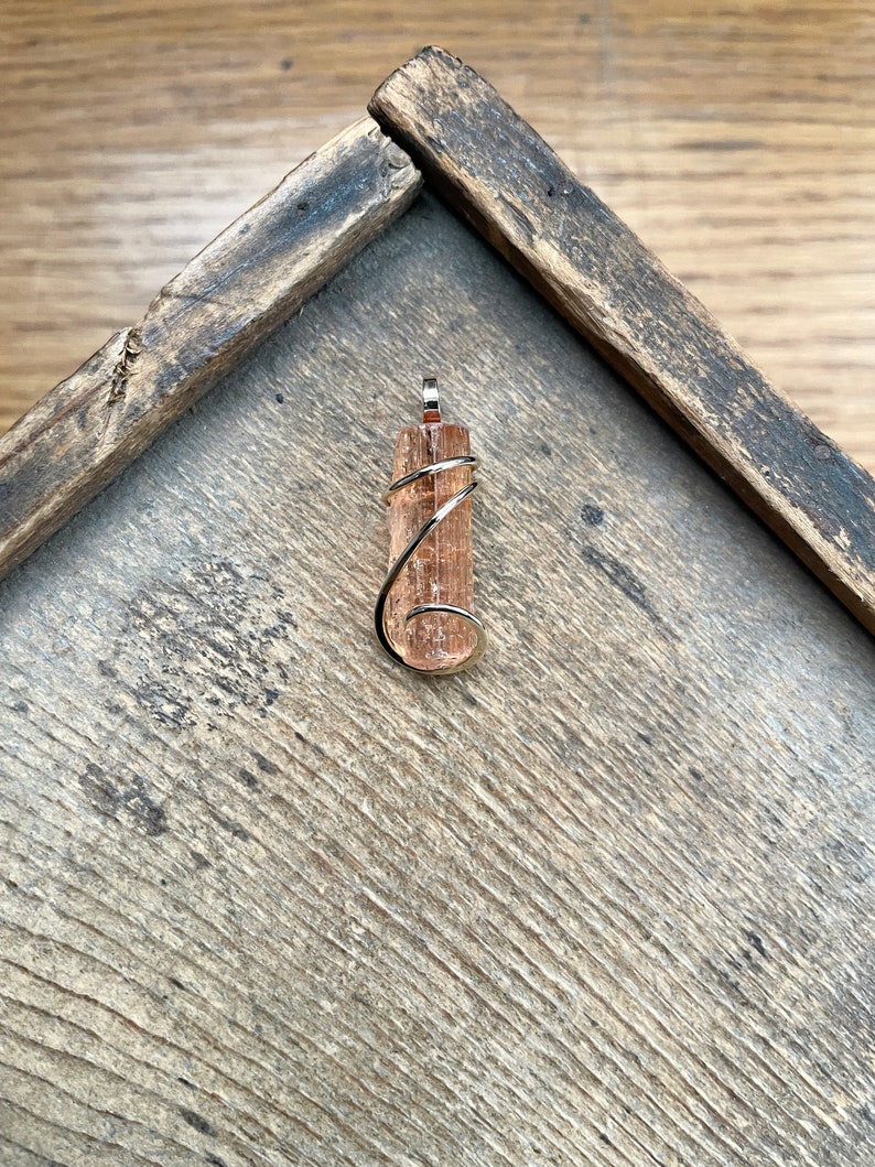 May include: A brown and white crystal pendant wrapped in silver wire. The pendant is on a wooden surface.