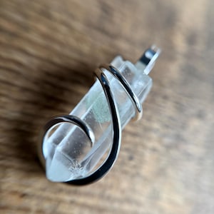 May include: A clear quartz crystal point wrapped in a silver wire pendant. The crystal has a small green inclusion.