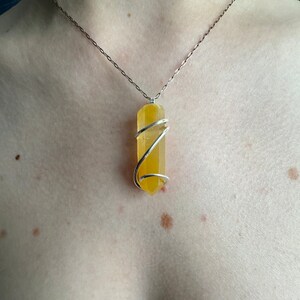 Pu&ograve; includere: Una collana a catena d'argento con un ciondolo di cristallo giallo avvolto in filo d'argento.