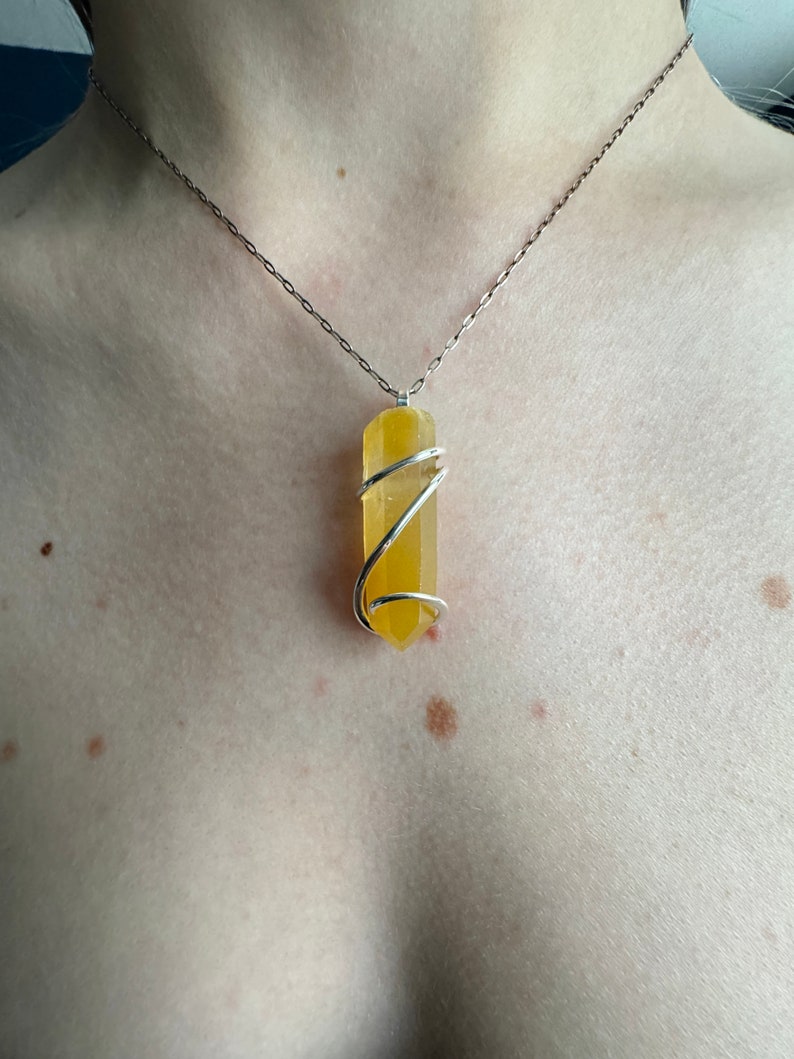 Pu&ograve; includere: Una collana a catena d'argento con un ciondolo di cristallo giallo avvolto in filo d'argento.