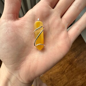 Pu&ograve; includere: Un ciondolo di cristallo giallo avvolto in filo d'argento. Il ciondolo ha la forma di un lungo rettangolo sottile con estremit&agrave; appuntite.