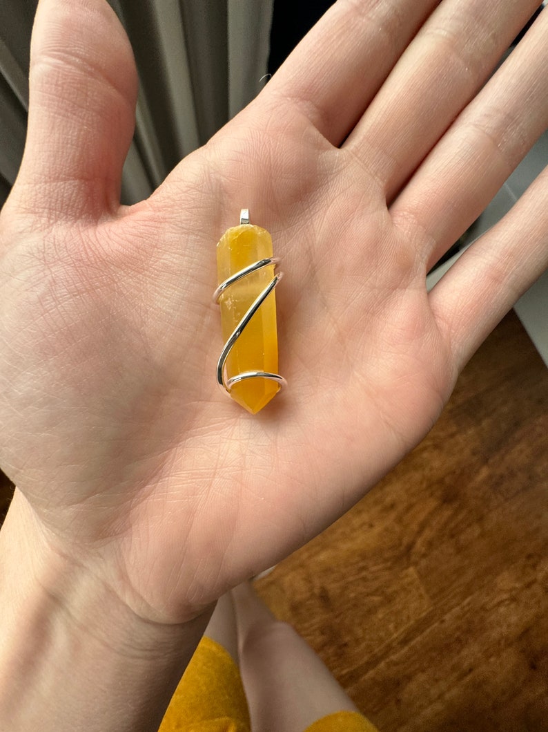 Pu&ograve; includere: Un ciondolo di cristallo giallo avvolto in filo d'argento. Il ciondolo ha la forma di un lungo rettangolo sottile con estremit&agrave; appuntite.