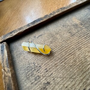 Pu&ograve; includere: Un cristallo giallo avvolto in filo d'argento. Il cristallo &egrave; su una superficie di legno.
