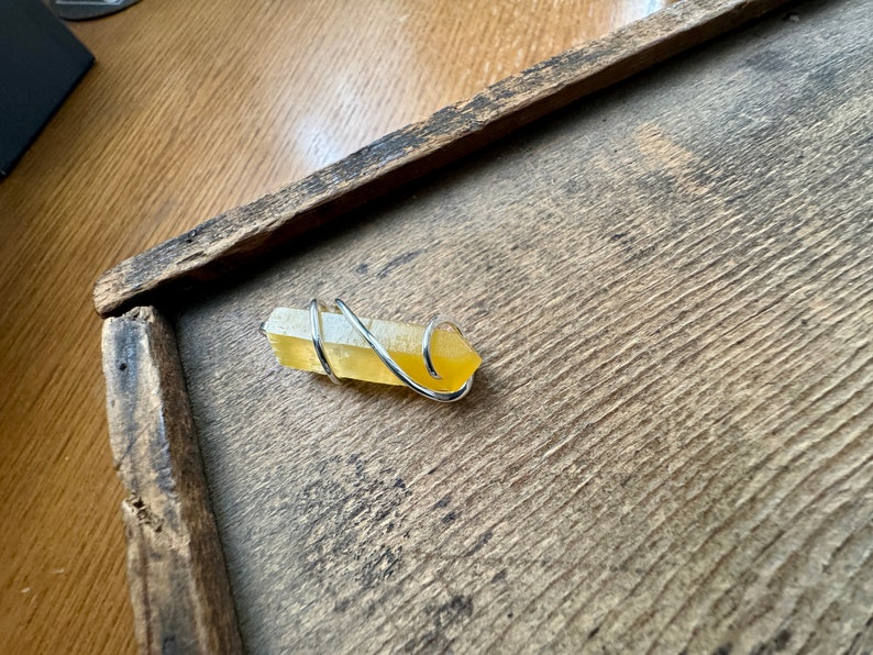 Pu&ograve; includere: Un cristallo giallo avvolto in filo d'argento. Il cristallo &egrave; su una superficie di legno.
