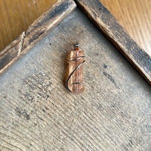 May include: A gold wire wrapped pendant featuring a natural, translucent, orange-brown crystal. The crystal is a long, thin, rectangular shape with a pointed end.