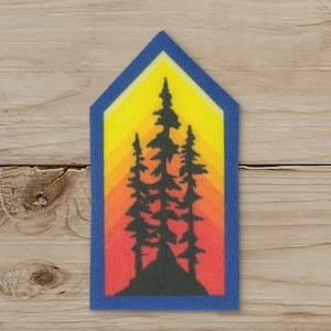 May include: A rectangular patch with a blue border and a stylized sunset design. The patch features a gradient of colors, transitioning from red at the bottom to yellow at the top, with black silhouettes of pine trees in the center.