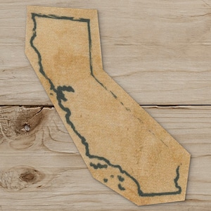 May include: A tan fabric tie shaped like the state of California, with a dark green outline. The tie has a distressed, vintage look, and is set against a wooden background.
