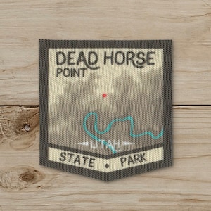 May include: A rectangular patch with the text "DEAD HORSE POINT" above a map outline and "UTAH STATE PARK" below. The patch has a gray background with a teal map outline and a red dot.