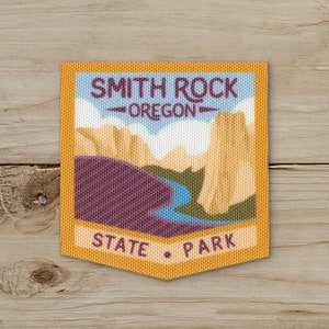 May include: A rectangular patch featuring the text "SMITH ROCK OREGON STATE PARK" in purple and white. The patch has a landscape design with tan rock formations, a blue river, and a purple foreground, all set against a light blue sky.