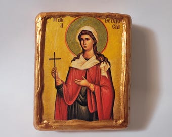 May include: A hand-painted icon of a woman holding a cross. The icon is framed in gold and has a yellow background with a green halo around the woman's head. The text "Hail" and "Theotokos" is written in Greek on the icon.