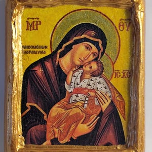 Può includere: Un'icona religiosa che raffigura la Vergine Maria che tiene in braccio il bambino Gesù. L'icona è dipinta su un pannello di legno e incorniciata in oro. Lo sfondo è giallo con un'aureola verde intorno alla testa di Maria. L'icona è iscritta con le parole "MP OY IC XC" in greco.