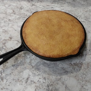 May include: A cast iron skillet with a golden brown cornbread inside.