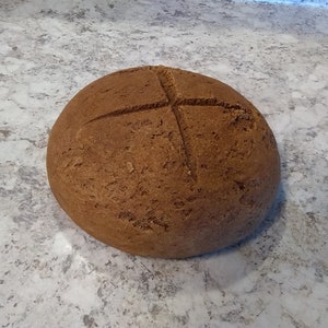 May include: A round loaf of brown bread with a cross-shaped cut on top.