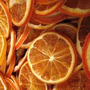 May include: A close-up of a pile of dried orange slices. The slices are arranged in a random pattern, with some overlapping. The orange slices are a deep orange colour and have a slightly translucent appearance.