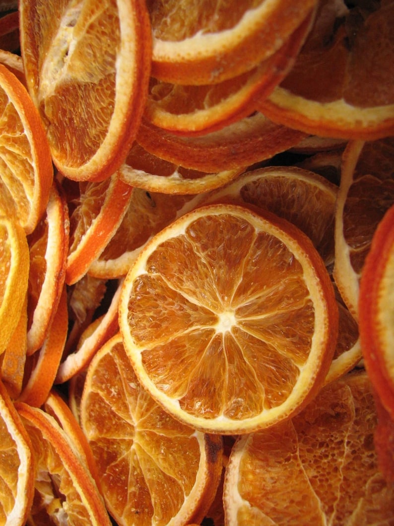May include: A close-up of a pile of dried orange slices. The slices are arranged in a random pattern, with some overlapping. The orange slices are a deep orange colour and have a slightly translucent appearance.