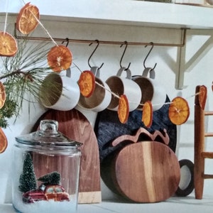 May include: A string of dried orange slices hangs from a white shelf in a kitchen. The string is decorated with dried orange slices and is hanging from hooks on the shelf. There are also white mugs hanging from the hooks.