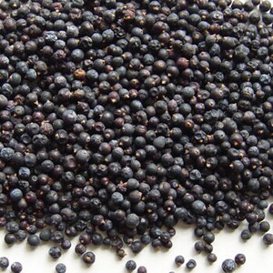 May include: A close-up view of a pile of dried juniper berries. The berries are dark blue and have a slightly wrinkled texture.