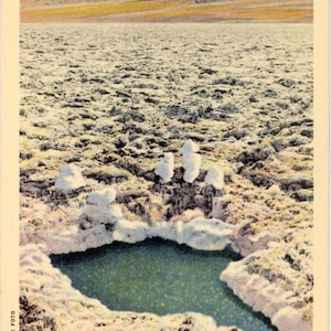 May include: Vintage postcard image of a salt pool in Death Valley, California. The pool is surrounded by white salt formations, with a backdrop of mountains and a blue sky. The text "D.V. 15 Salt Pool in Salt Beds, Telescope Peak in Distance" is visible.