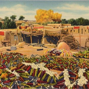 May include: Vintage postcard depicting a Southwestern village scene. The image shows adobe buildings, a horse-drawn cart, and a large pile of colorful corn cobs in the foreground. The sky is a light blue.