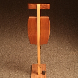 May include: A wooden stand with two rectangular shelves and a base. The stand is made of light and dark wood and has a simple design.