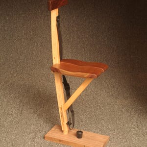 May include: A wooden folding chair with a brown seat and a black strap. The chair is made of light and dark wood and has a simple design.