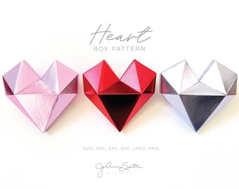 May include: Three origami heart boxes in pink, red, and silver. The boxes are made of paper and have a geometric design. The text "Heart Box Pattern" is above the boxes. The text "SVG, PDF, EPS, DXF, JPEG, PNG" is below the boxes. The text "Jam Guita Designs" is at the bottom of the image.