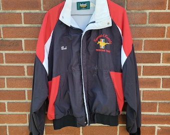 May include: Black, red, and white windbreaker jacket with a zipper closure. The jacket has a white collar and a white stripe down the sleeves. The jacket has an embroidered logo that says "Squad & Rattle Prevention Team" with a horse and rider graphic. The jacket also has the name "Bob" embroidered on the left chest.