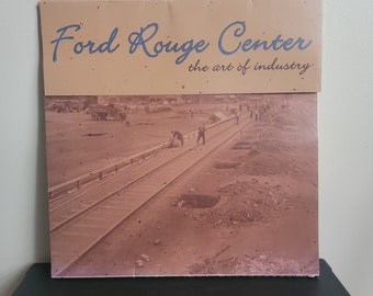 May include: A vintage photograph of a train track with workers in the background. The image is titled "Ford Rouge Center, the art of industry".