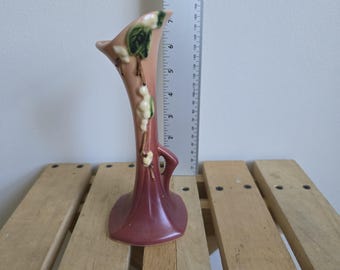 May include: A vintage ceramic vase in shades of pink and burgundy, adorned with a botanical design. The vase has a tall, slender shape with a flared top and a decorative handle. The vase is approximately 8 inches tall.