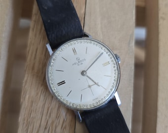 May include: A silver wristwatch with a white face and black leather band. The watch face has a silver rim with small diamonds around the edge. The watch face has black Roman numeral hour markers and the text "Helbros Swiss" printed on it.