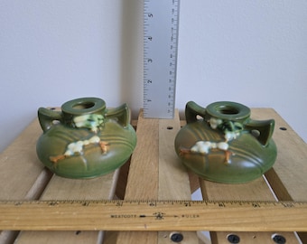 May include: Two green ceramic vases with handles and floral accents. The vases are on a wooden surface with a ruler and measuring tape in the background. Each vase is approximately 4 inches wide.