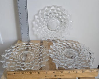 May include: Three clear glass plates with a diamond pattern and scalloped edges. The plates are arranged on a wooden surface with a ruler measuring up to 12 inches. The plates have a central, textured design.
