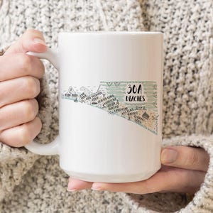 May include: A white ceramic mug featuring a graphic illustration of the 30A coastline. The design includes the text 30A BEACHES and lists various beach locations along the Florida coast with small icons of palm trees and buildings.